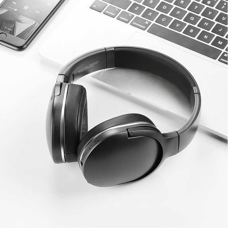 Baseus Encok D02 PRO wireless headphones placed next to a laptop and smartphone for work and music use